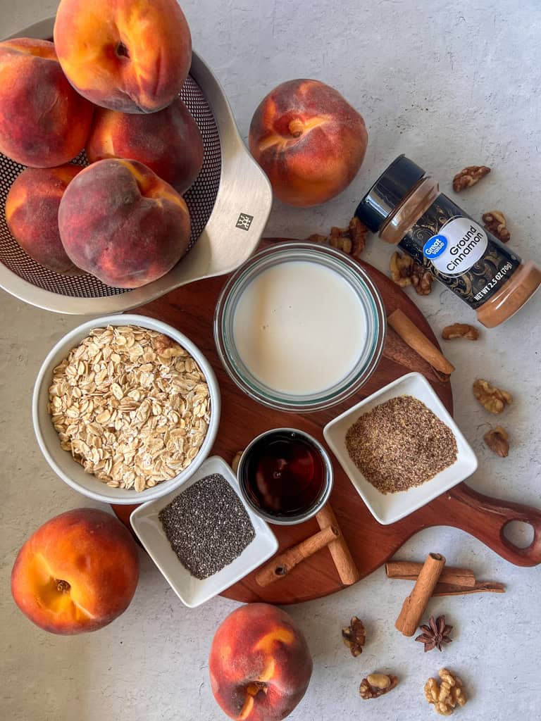 Ingredients for peach overnight oats laid out on the table, peaches, cinnamon, almond milk, oats in a bowl and cinnamon.
