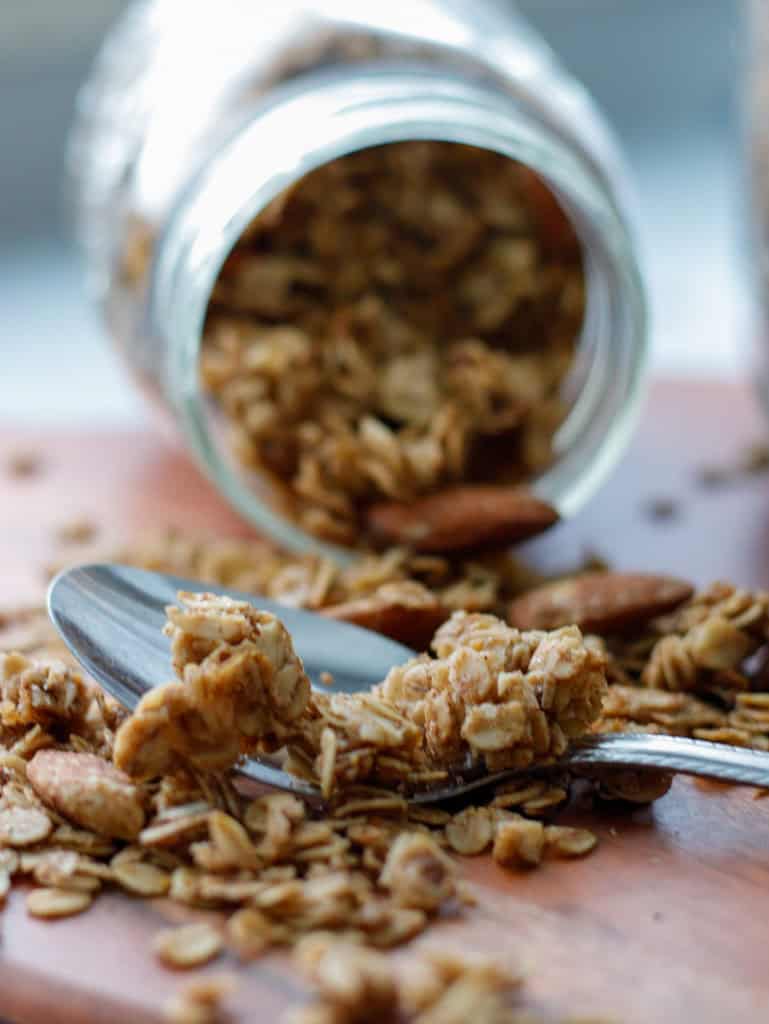 Granola spilling out of a mason jar onto the table with a spoon