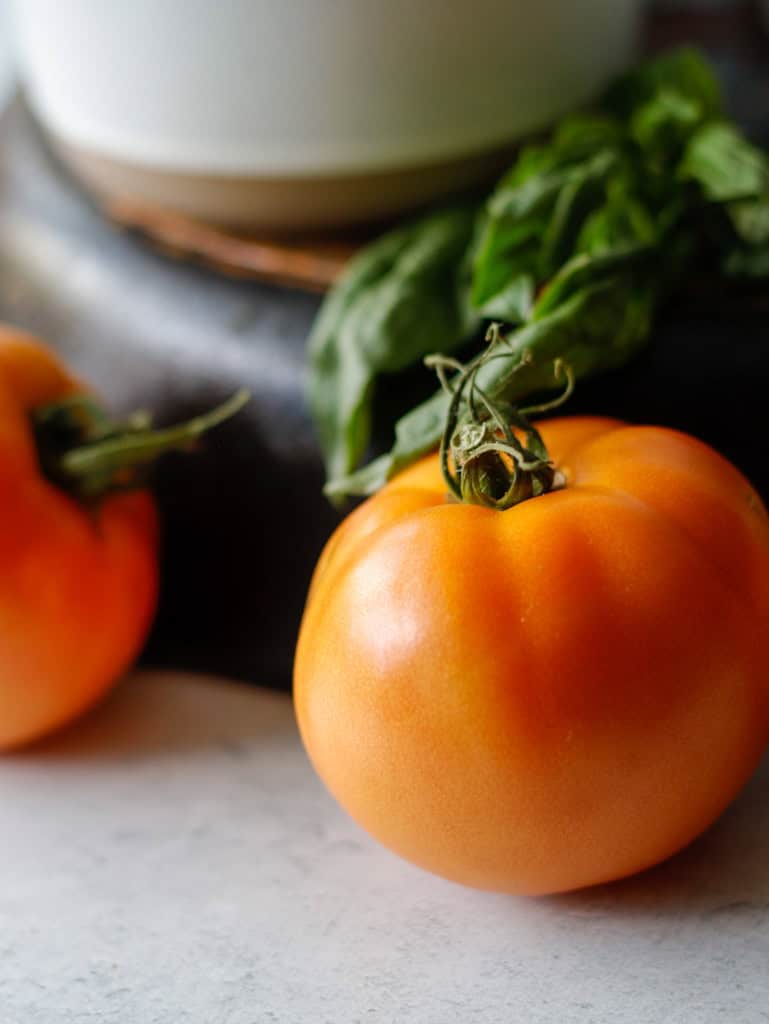 Fresh heirloom tomatoes with green leaves on a rustic surface, focusing on healthy, organic produce for gourmet cooking and food photography.