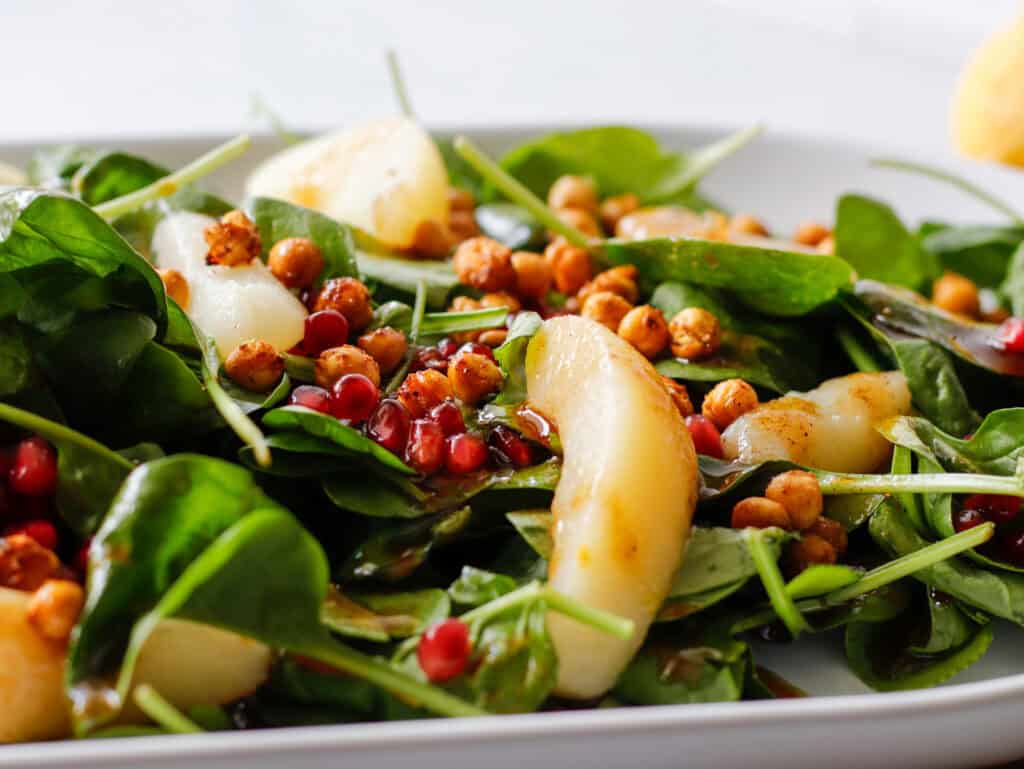 Bed of spinach on a plate close up on pears and pomegranates.