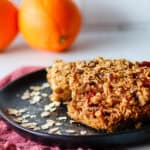 Stacked simple oatmeal bars on a black plate with oranges in the background.