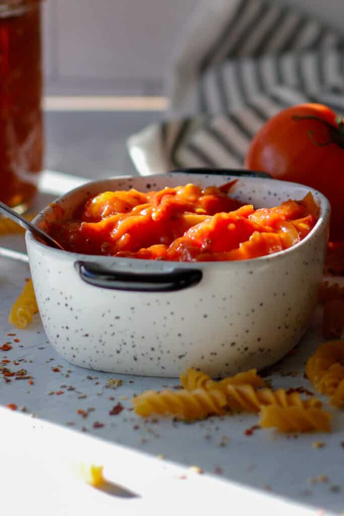 White bowl filled with homemade tomato sauce with dried pasta ready to cook.