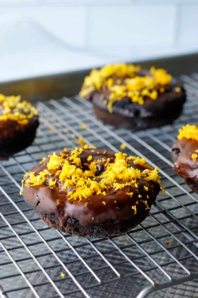 Double Chocolate donuts with orange zest on top on a wire baking rack.