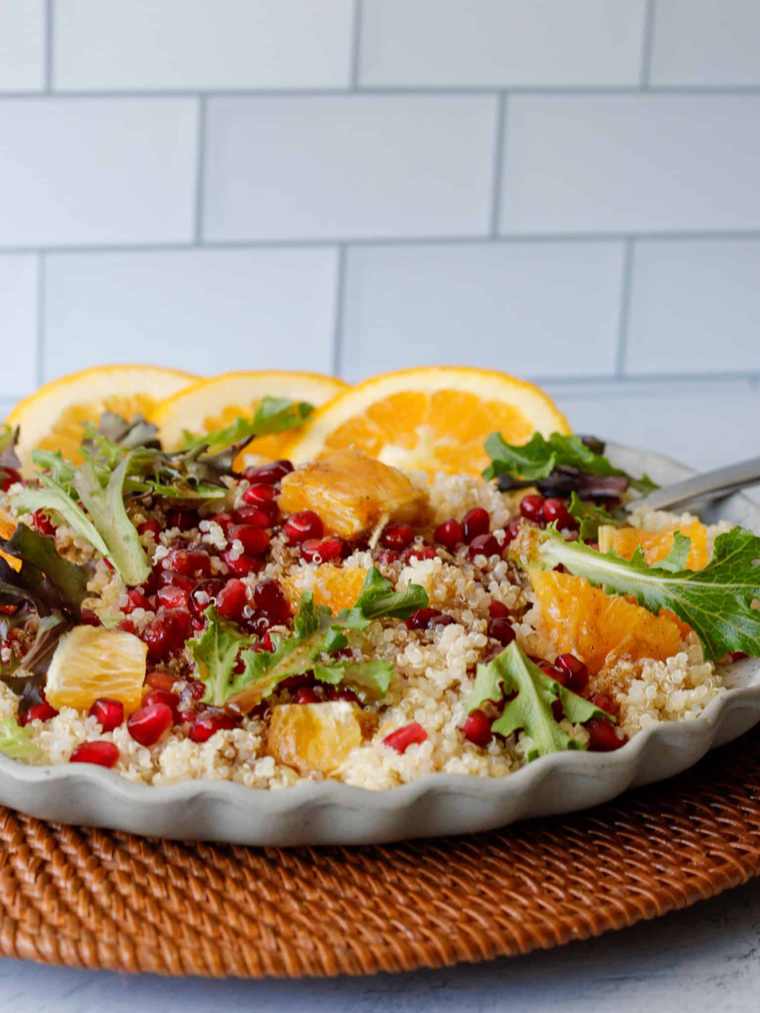Quinoa salad on a playe with bright red pomegranate seeds, oranges and greens.
