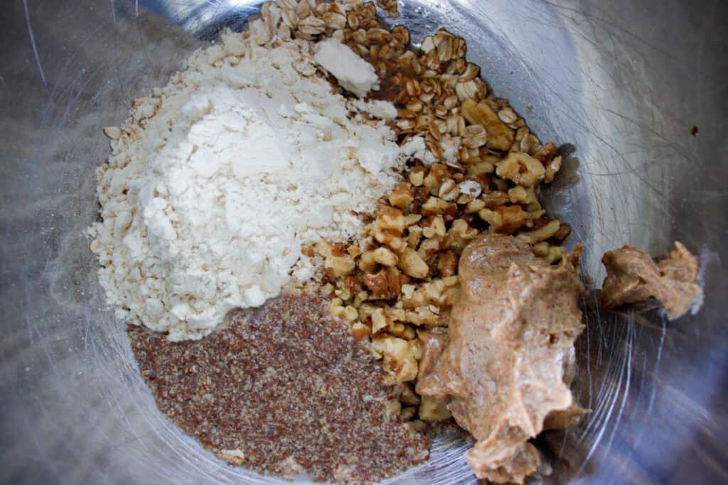 Mixing bowl filled with almond butter, protein powder, flax seed, oats and nuts