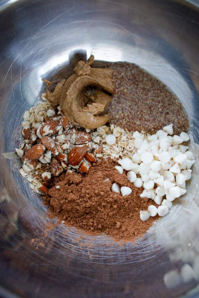 Almond, white chocolate, cocoa powder, spices, and dried fruit ingredients in stainless steel bowl for baking or cooking.
