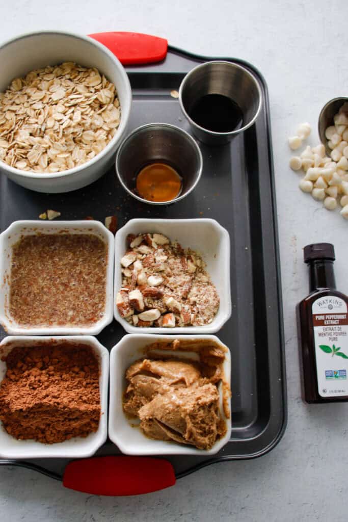 Cream of oats, honey, vanilla, peanut butter, and cocoa powder ingredients for healthy oatmeal recipes on a black tray.
