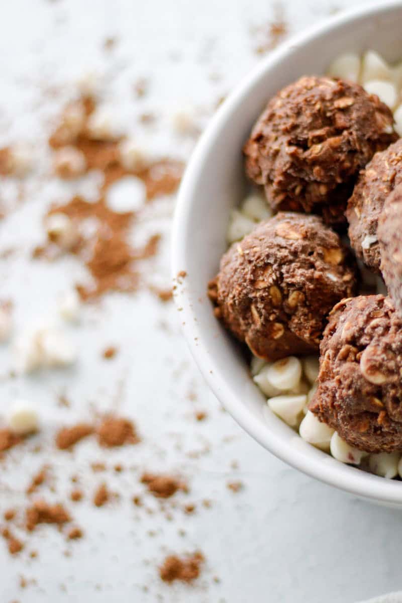 View of half of a white bowl filled with chocolate peppermint oat balls and white chocolate chips