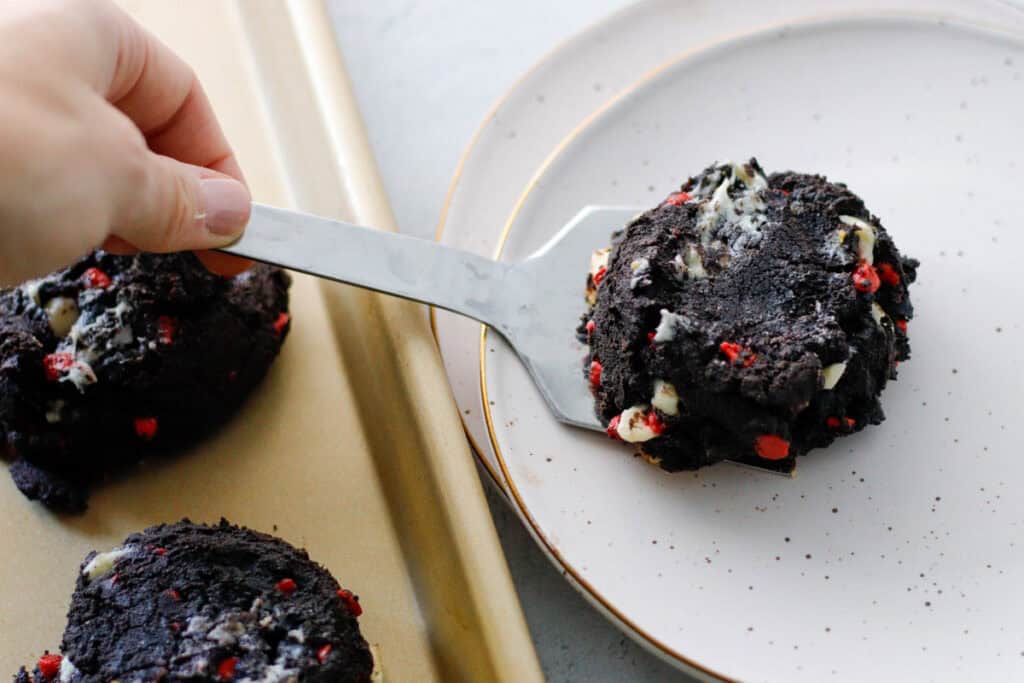 hand serving up cookies from a baking sheet to a plate