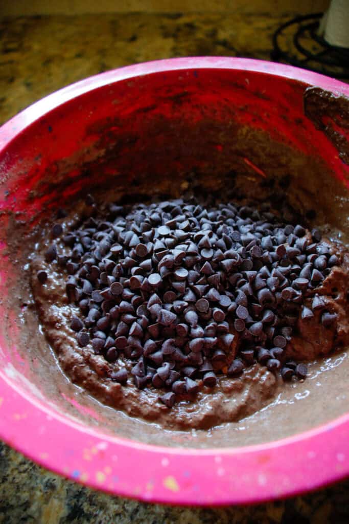 Pink mixing bowl with chocolate muffin batter and chocolate chips