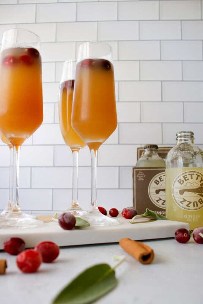 4 champagne flutes filled with ginger apple fizz mocktail and cranberries