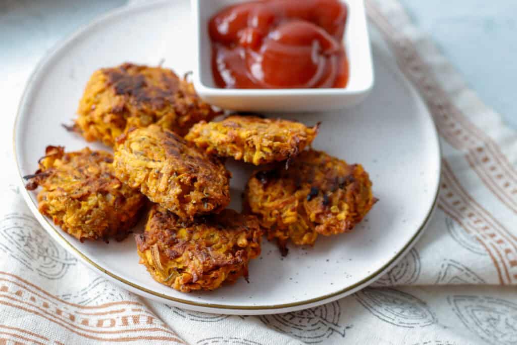 Crispy sweet potato hash brown circles on a plate with a side of ketchup