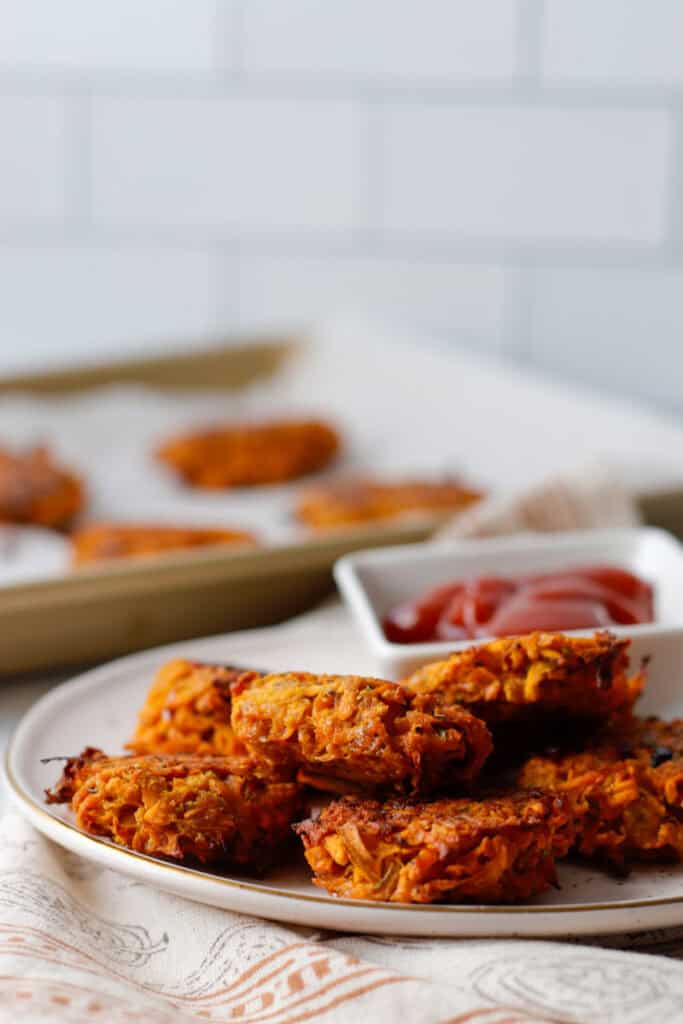 Easy hot honey sweet potato hash browns on a white plate with a side of ketchup and a baking sheet in the background