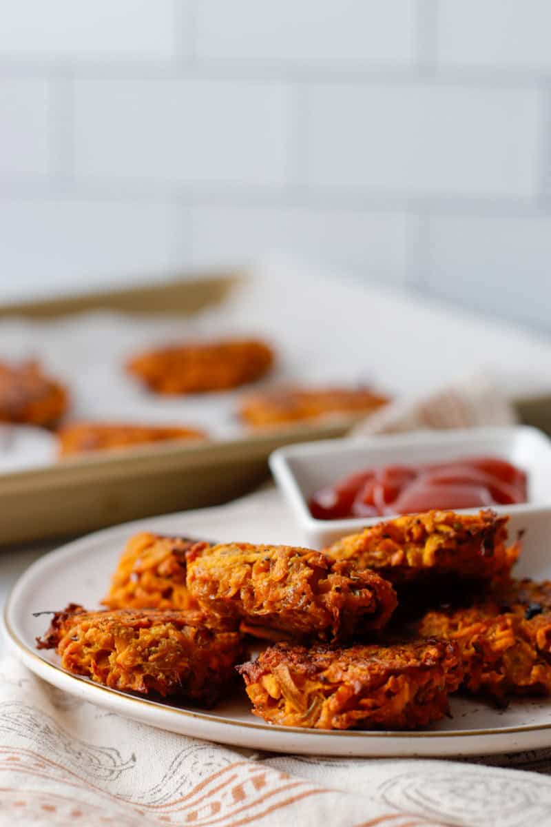 Easy hot honey sweet potato hash browns on a white plate with a side of ketchup and a baking sheet in the background