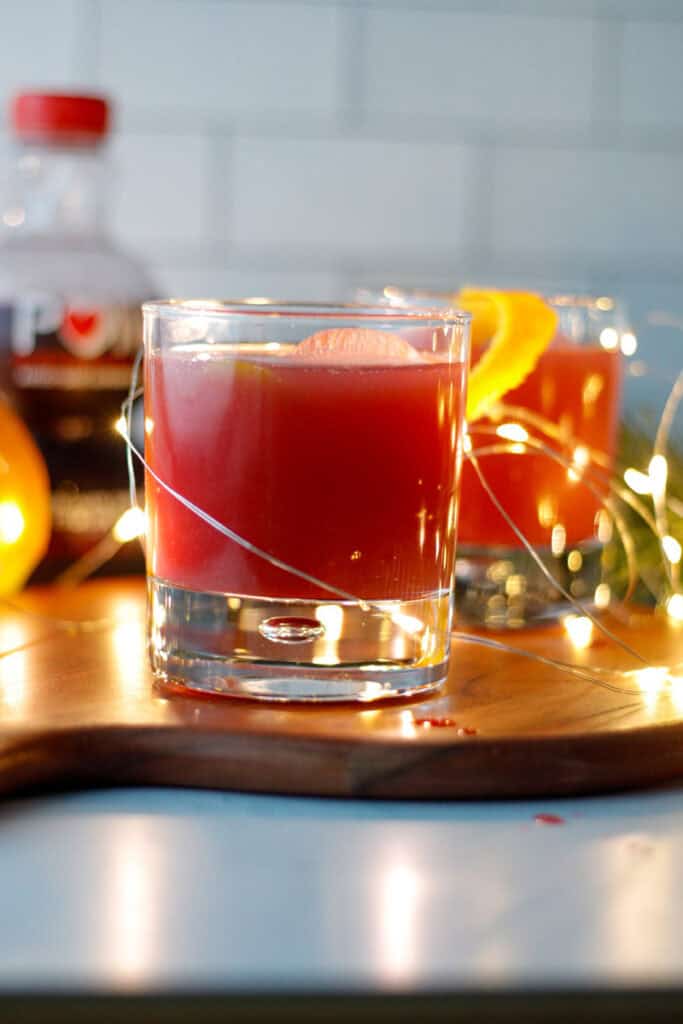Sparkling orange pomegranate drink for the holidays on a tray with christmas lights