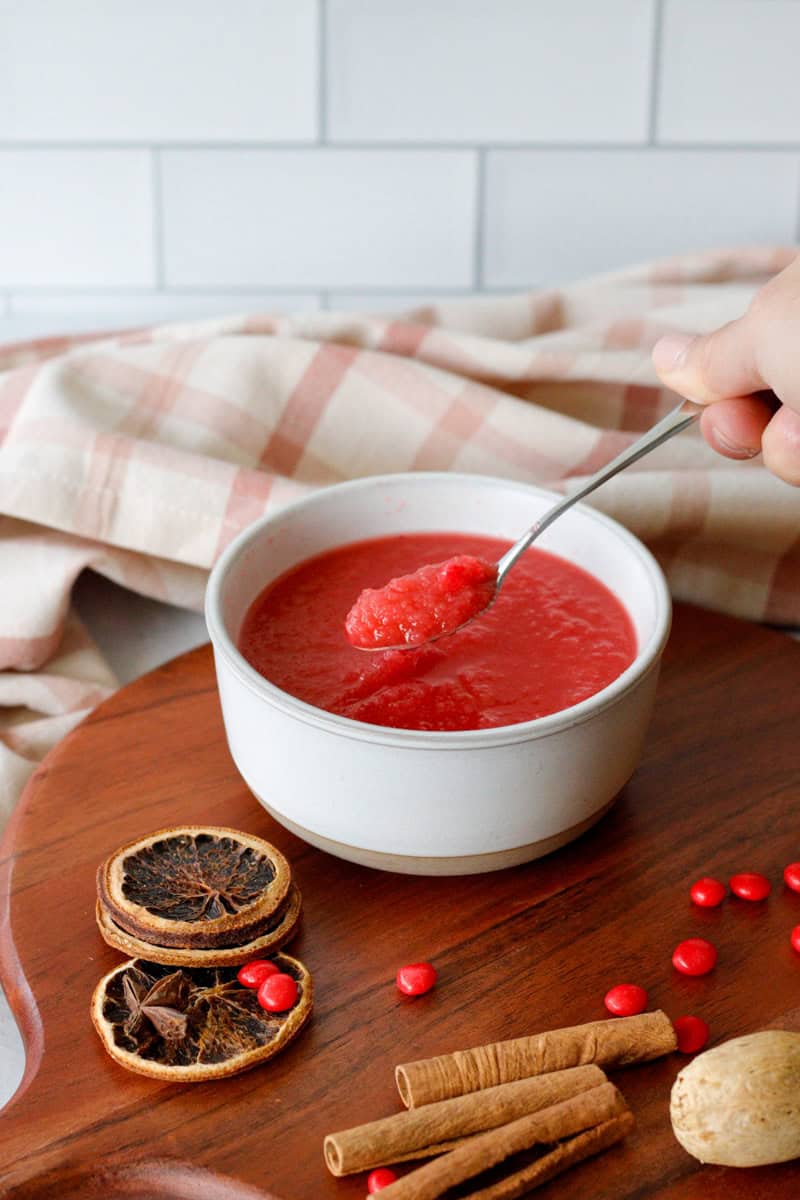 bowl of bright red apple sauce with a hand grabbing a spoon full