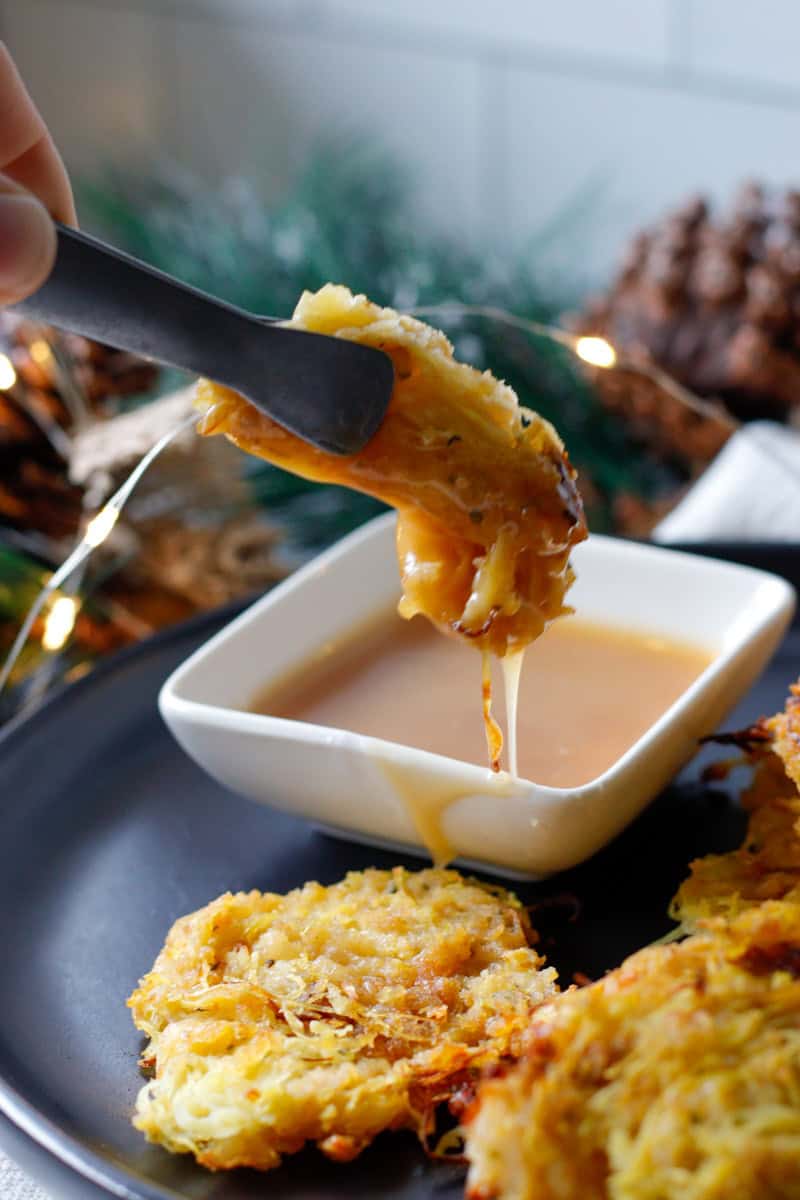 Picking up spaghetti squash bites with serving tongs and dipping them in maple aoli