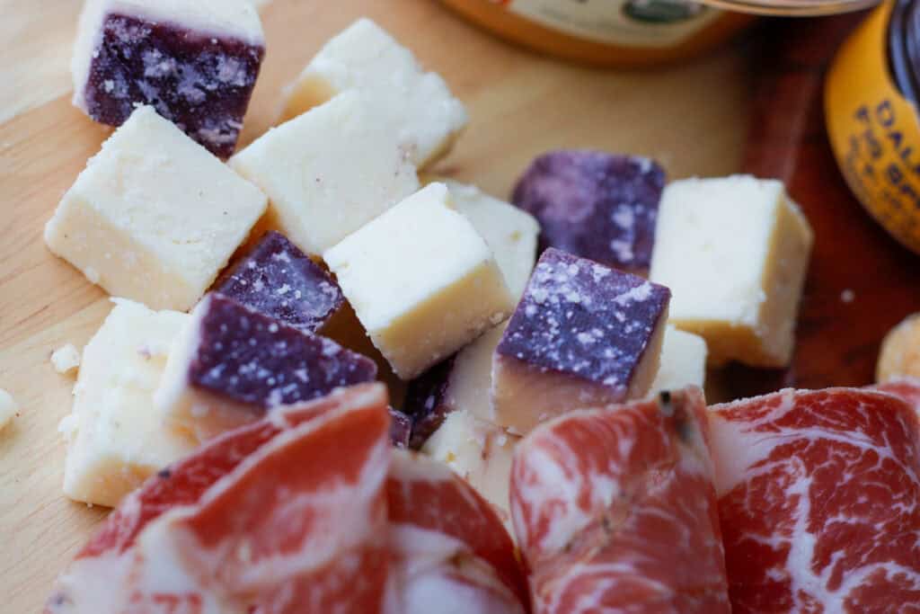 Merlot cheese, with a purple ring on a cheese board next to cured meat