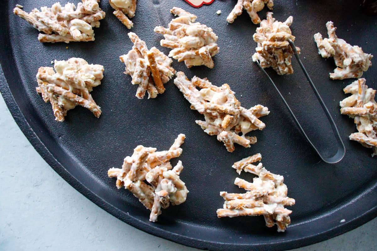 pretzel and peanut stacks on a black serving tray with serving tongs