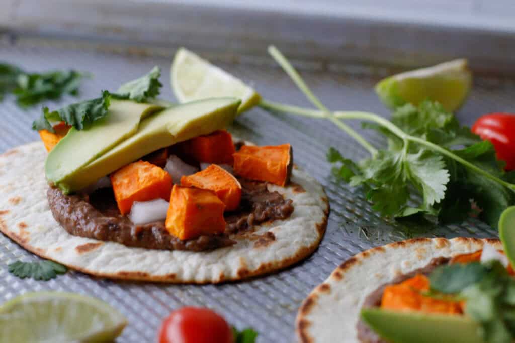Crispy tortilla on a baking dish topped with black bean, sweet potato, avocado and cilantro
