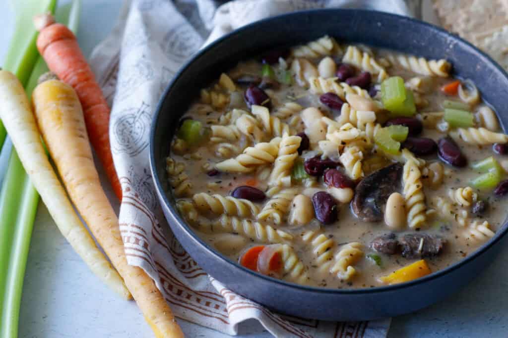 vegan vegetables and bean soup in a bowl with banza noodles with a napkin and rainbow carrots on the side