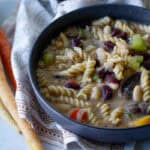 vegan vegetables and bean soup in a bowl with banza noodles with a napkin and rainbow carrots on the side