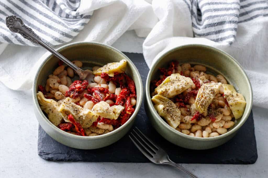 Ingredients for Mediterranean White Bean Skillet arranged on a countertop, including white beans, marinated artichokes, sundried tomatoes, and seasonings. Perfect for a quick and easy vegetarian meal.