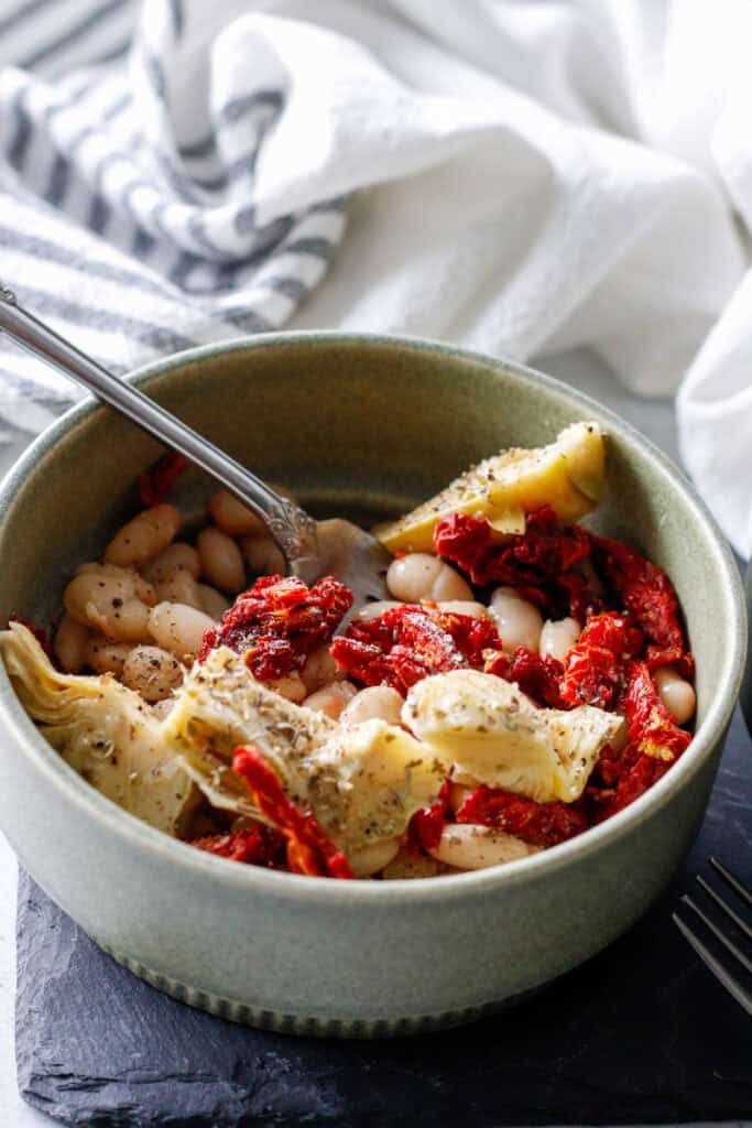 Creamy white beans with sun-dried tomatoes and roasted artichoke hearts in a rustic bowl, showcasing a healthy and flavorful plant-based dish perfect for nutritious meals.