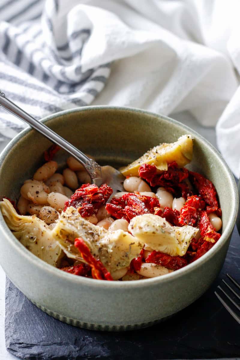 Creamy white beans with sun-dried tomatoes and roasted artichoke hearts in a rustic bowl, showcasing a healthy and flavorful plant-based dish perfect for nutritious meals.