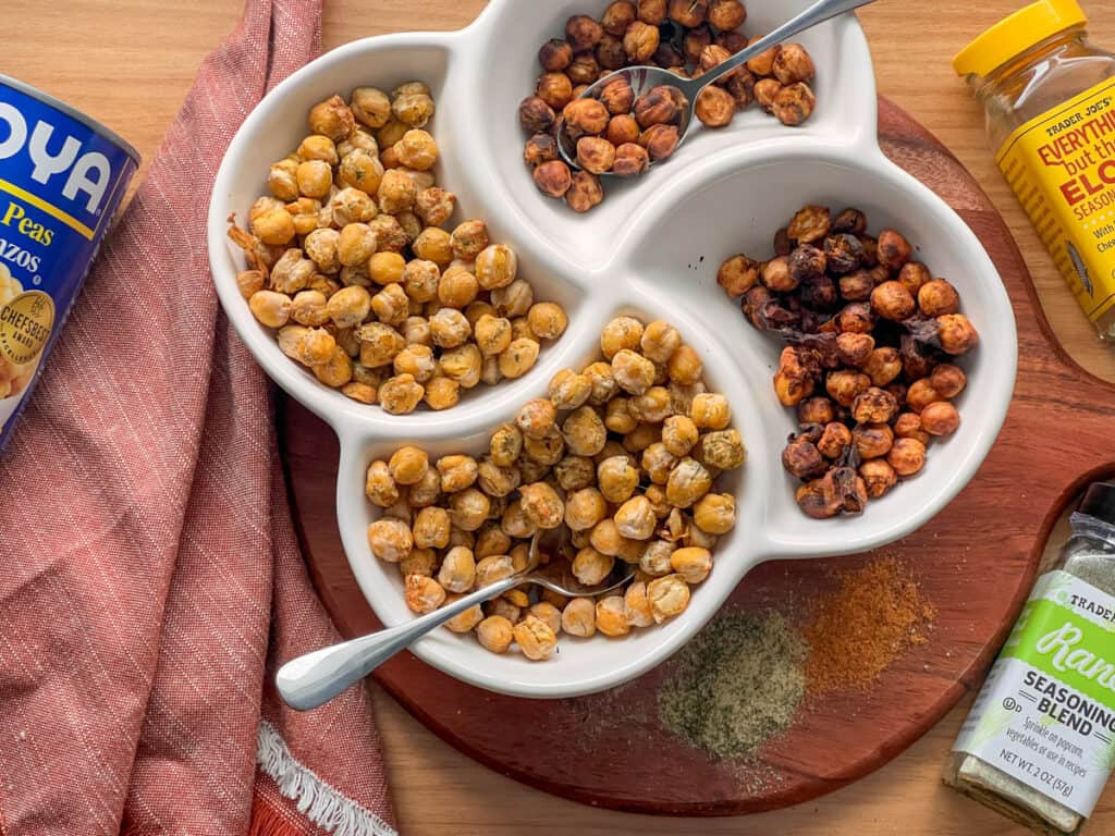 Overhead of crispy chickpeas in a four section bowl on a brown cutting board, with a napkin and seasoning bottles scattered.
