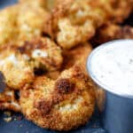 Breaded cauliflower bites on a plate with a side of dipping sauce
