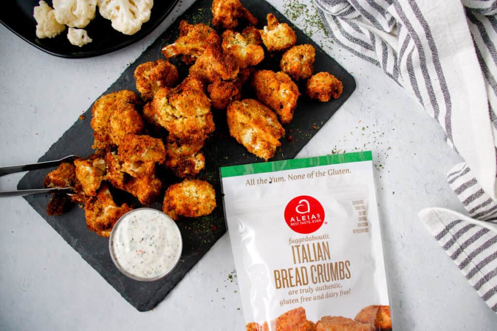 Overhead view of Air fried cauliflower bites on a platter with dressing and an Aleia's Italian Bread Crumbs bag.