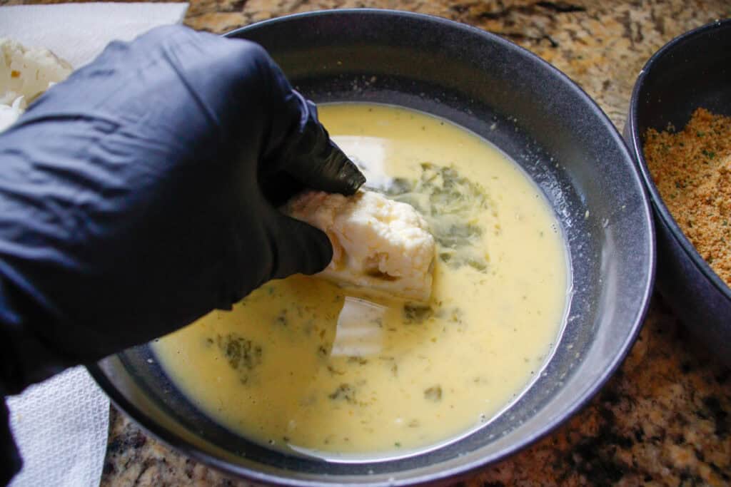 Person tossing cauliflower in egg wash to prepare for breading
