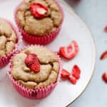 three strawberry cheesecake muffins on a plate with dried strawberries scattered