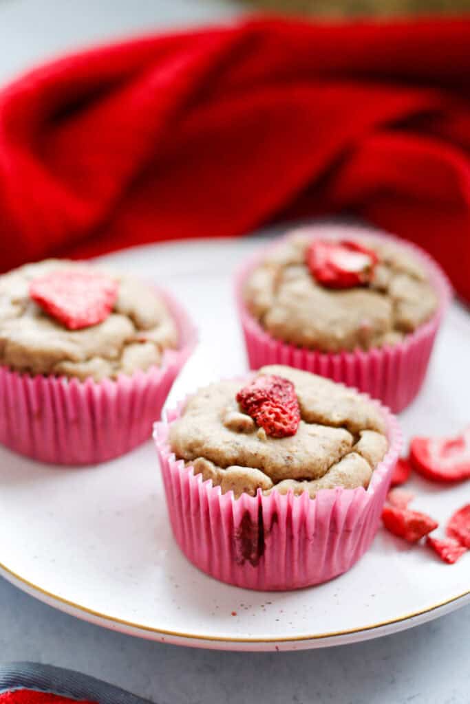 three strawberry cheesecake muffins on a plate with dried strawberries scattered