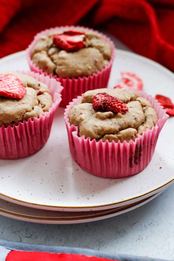 three strawberry cheesecake muffins on a plate with dried strawberries scattered