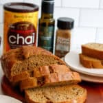 Sliced bread loaf on a platter, with olive oil and pumpkin spice in the background and a plate with sliced bread to the side.