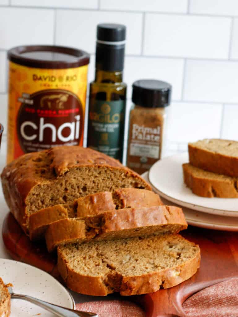 Sliced bread loaf on a platter, with olive oil and pumpkin spice in the background and a plate with sliced bread to the side.