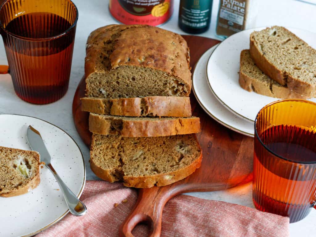 overhead of sliced pumpkin bread loaf with stacked slices on plates and amber mugs of tea
