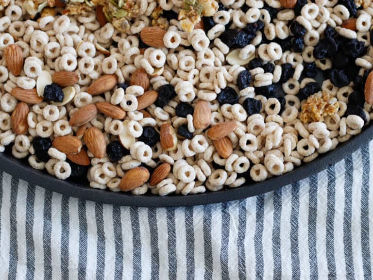 Almonds, blueberries, and toasted cereal mix in a black tray on a striped cloth background.