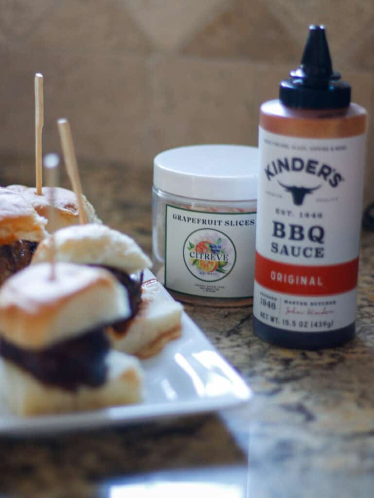 Creamy BBQ sauce bottle, grapefruit slices container, and delicious food appetizers on a rustic wooden table. Perfect for food photography emphasizing condiment and snack presentation.