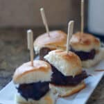 Cream-filled mini sliders with beef patties and soft buns on a white serving dish, ideal for gourmet food tasting, food photography, and appetizer presentation. Perfect for food lovers and culinary enthusiasts.
