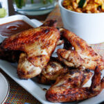 Chicken wings displayed on a white plate with corn dish in a bowl in the background