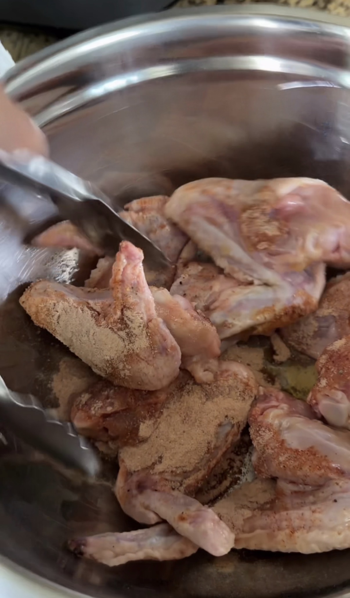 Naked wings in a bowl being tossed with seasoning