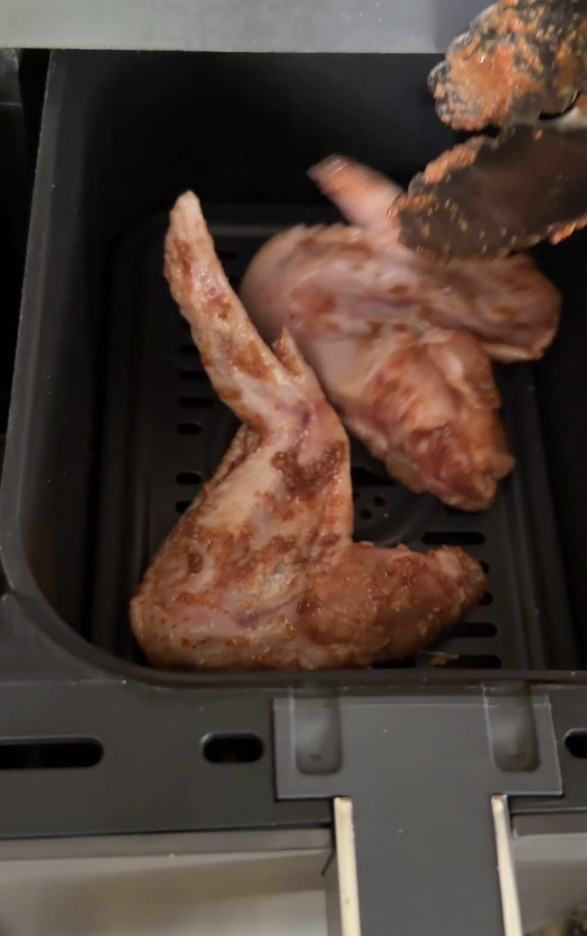 Seasoned wings being placed in the air fryer