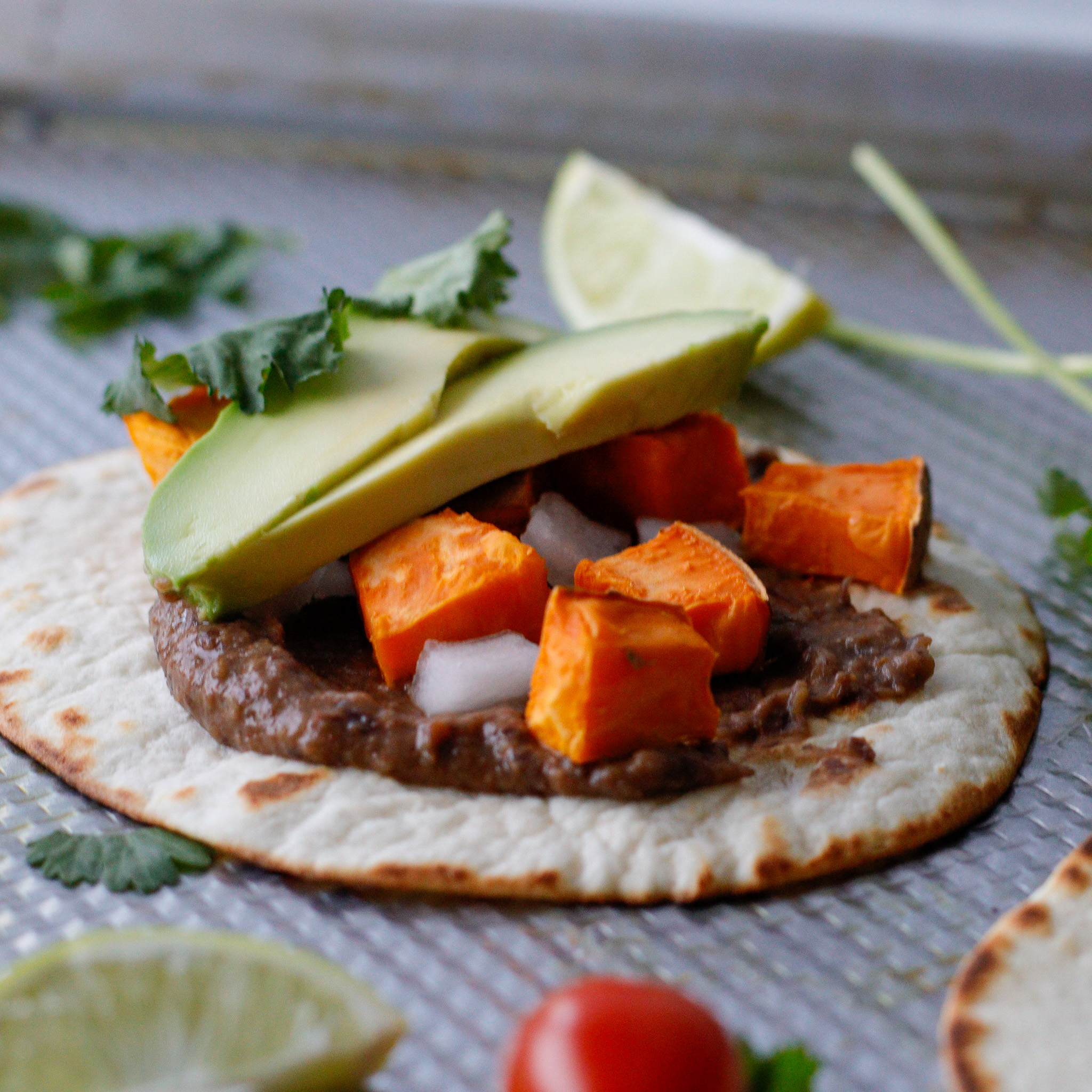 Tortilla on a sheet pan topped with beans, sweet potato, avocado and cilantro